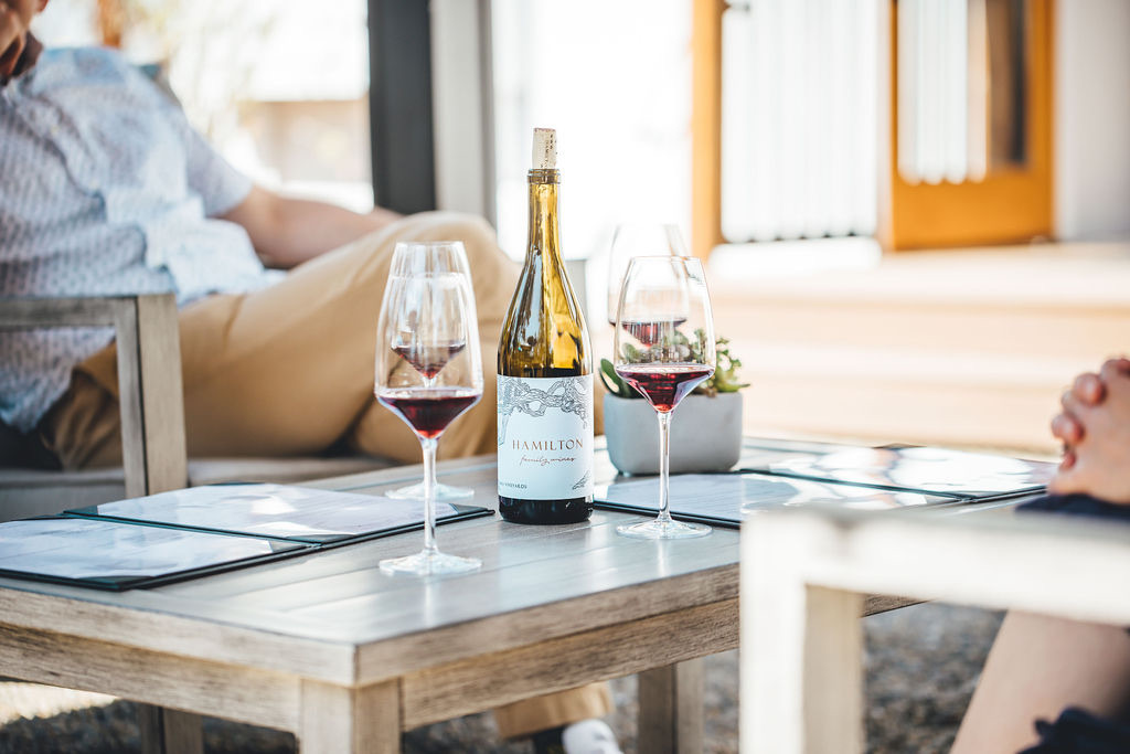 Hamilton Family Wines bottle and glasses on a low outdoor table.