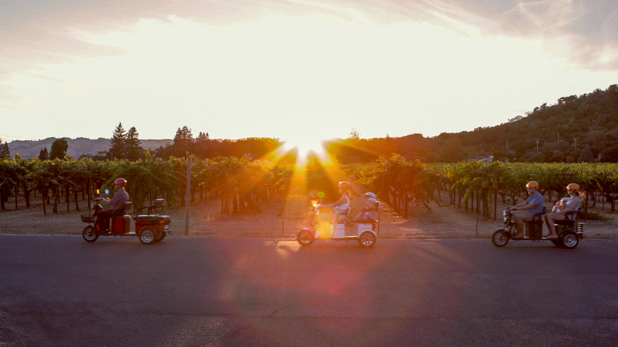 Electric trike riders passing a Kenwood vineyard at sunset